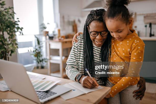 niña de pie junto a su madre escribiendo en un libro en casa - working mother fotografías e imágenes de stock