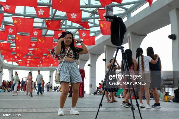 Woman films a dancing video under flags of Hong Kong and China at Central Ferry Piers in Hong Kong on July 2 a day after the city marked the 26th...