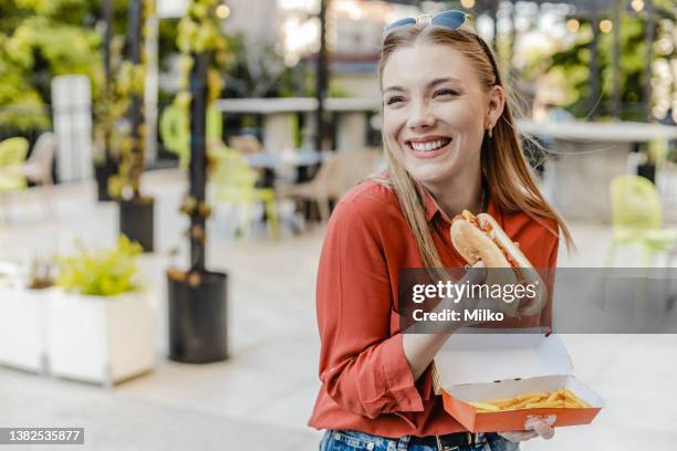 mujer joven comiendo perrito caliente y sonriendo - frankfurt fotografías e imágenes de stock