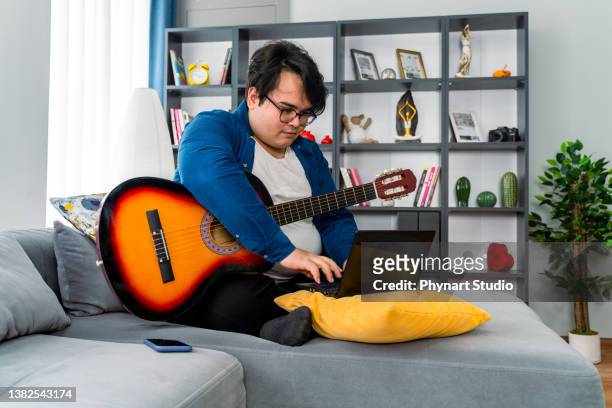 overweight boy learning online how to play guitar - chubby arab stock pictures, royalty-free photos & images