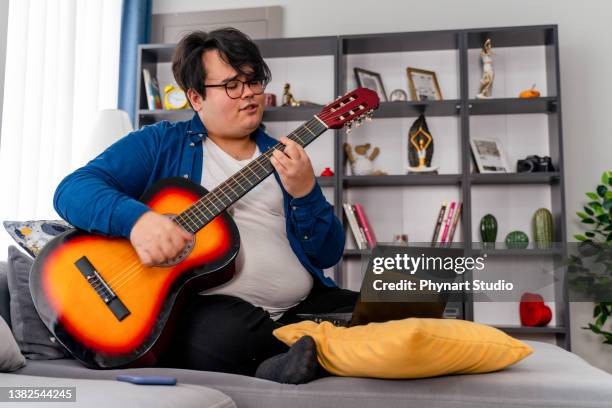 niño con sobrepeso aprendiendo en línea a tocar la guitarra - chubby boy fotografías e imágenes de stock