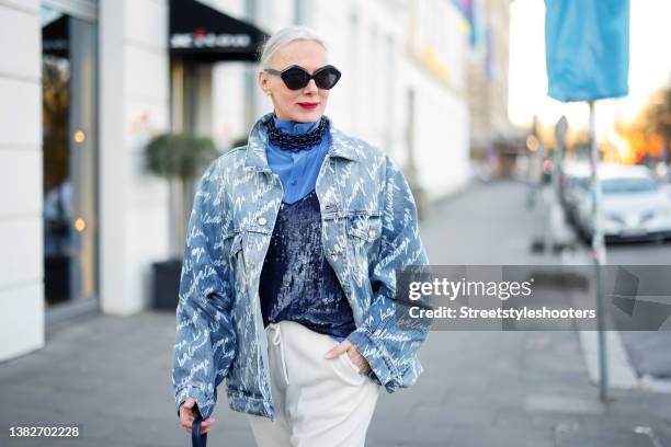 Best Ager Model and Influencer Petra van Bremen wearing a light blue denim jeans jacket with white all over logo print by Balenciaga, a blue blouse...