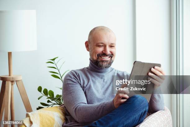 smiling mature man holding a digital tablet, sitting in the living room - website design stock pictures, royalty-free photos & images