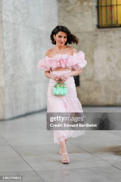 Alexandra Pereira wears silver and rhinestones earrings, a pale pink ruffled embroidered flower shoulder-off / short sleeves cropped top, a pale pink...