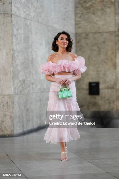 Alexandra Pereira wears silver and rhinestones earrings, a pale pink ruffled embroidered flower shoulder-off / short sleeves cropped top, a pale pink...