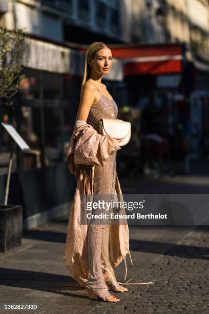Leonie Hanne wears gold earrings, a beige tulle with embroidered rhinestones / studded V-neck / tank-top jumpsuit, a beige embossed pattern oversized...