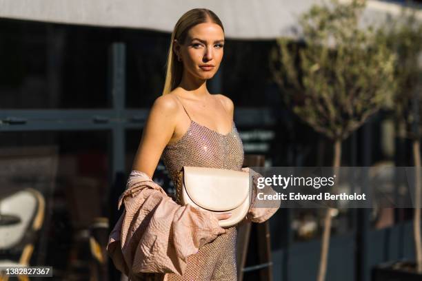 Leonie Hanne wears gold earrings, a beige tulle with embroidered rhinestones / studded V-neck / tank-top jumpsuit, a beige embossed pattern oversized...