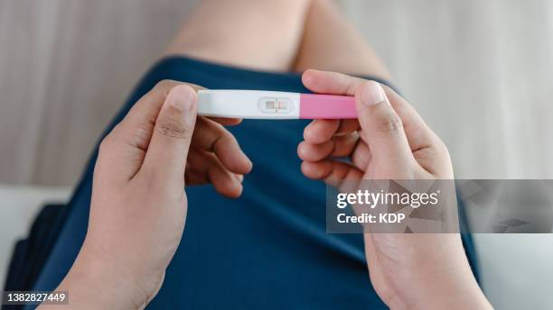 close-up of young woman hands holding a pregnancy test kit and waiting for positive result in her bedroom. - ovulation stock-fotos und bilder