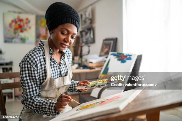 artista femenina afro con sombrero tradicional africano 
 y delantal, dibujo en estudio de arte - painter artist fotografías e imágenes de stock