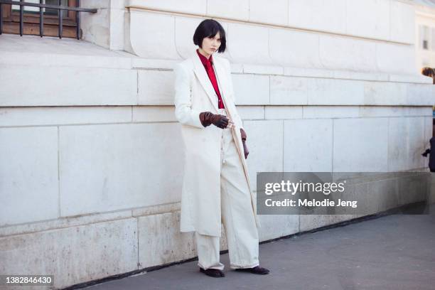 Model Steinberg wears a long white suit coat, white pants, red shirt, red tie, brown fingerless leather gloves, and black shoes at the Louis Vuitton...