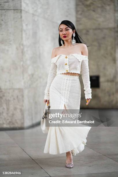 Jessica Wang wears large silver and crystal pendant earrings, a white cut-out / shoulder-off / gold buttons Long sleeves cropped top, a matching...