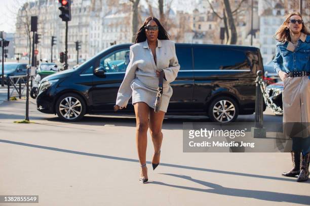 Honey Dijon wears a gray dress, black heels, and Christian Dior bag at the Sacai show at Hotel de Ville during Paris Fashion Week Fall/Winter 2022 on...