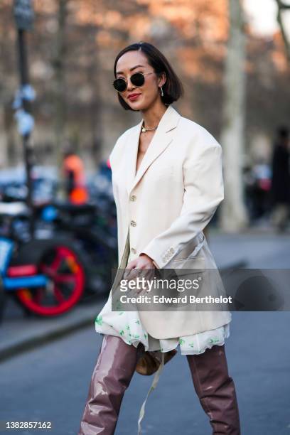 Chriselle Lim wears black circle sunglasses, silver and rhinestones earrings, a rhinestones and large pearl pendant necklace, a white latte long...