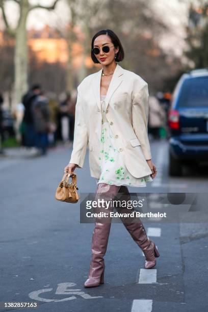 Chriselle Lim wears black circle sunglasses, silver and rhinestones earrings, a rhinestones and large pearl pendant necklace, a white latte long...