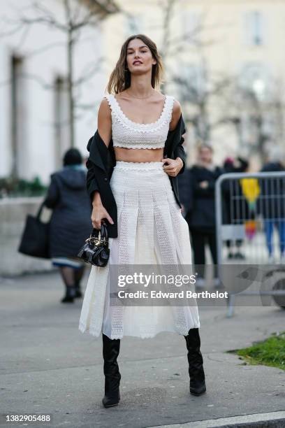Ophelie Guillerman wears a gold necklace, a white cut-out print pattern V-neck / cropped top, a matching high waist white cut-out print pattern /...