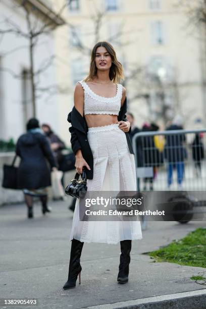 Ophelie Guillerman wears a gold necklace, a white cut-out print pattern V-neck / cropped top, a matching high waist white cut-out print pattern /...