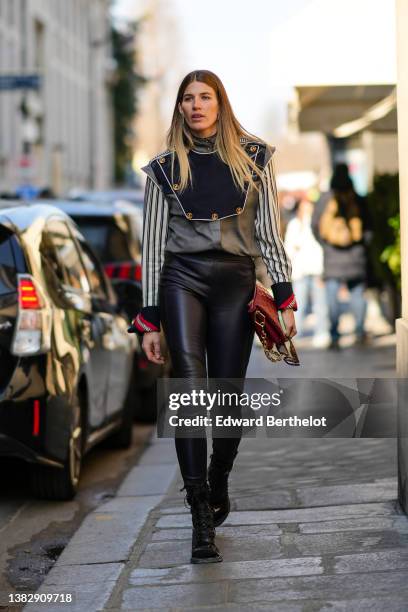 Veronika Heilbrunner wears a gray high neck jacket with black and white striped pattern sleeves and navy blue check yoke with gold buttoned shirt...