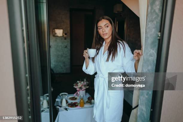 woman drinking coffee and looking through the hotel room window - luxury home dining table people lifestyle photography people stock pictures, royalty-free photos & images