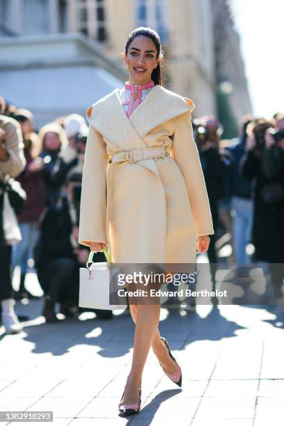 Jessica Kahawaty wears a beige yellow Hoodie Wrap belted coat from Louis Vuitton, a gray LV monogram print pattern and pale pink leather borders...