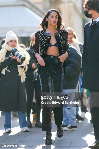 Laura Harrier wears a black velvet triangle bra underwear, a black with red and white print pattern jacket from Louis Vuitton, a shoulder bag, high...