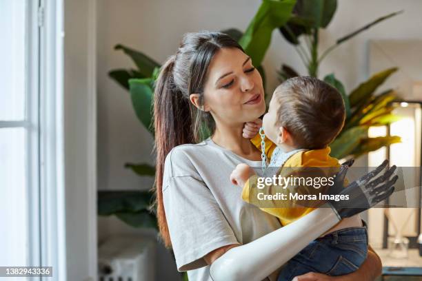 smiling mother with toddler standing at home - prothesen stockfoto's en -beelden