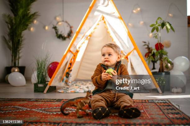 cute little baby boy sitting on the ground and playing with his dino toy - wigwam stock-fotos und bilder