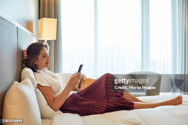 businesswoman using mobile phone on bed in hotel - south african woman stock pictures, royalty-free photos & images