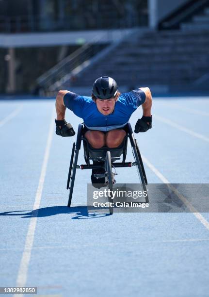 focused male wheelchair athlete training on sunny blue sports track - training wheels fotografías e imágenes de stock