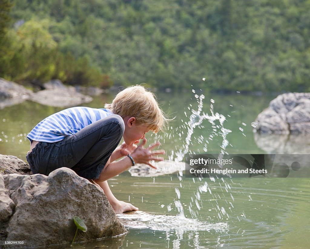 Boy washing his face in still lake