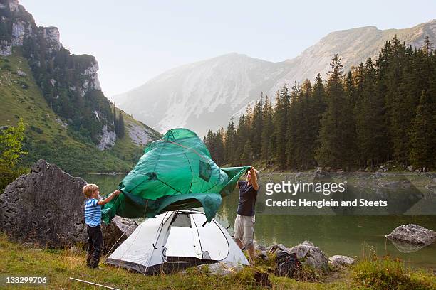 father and son pitching a tent by lake - plane stock-fotos und bilder