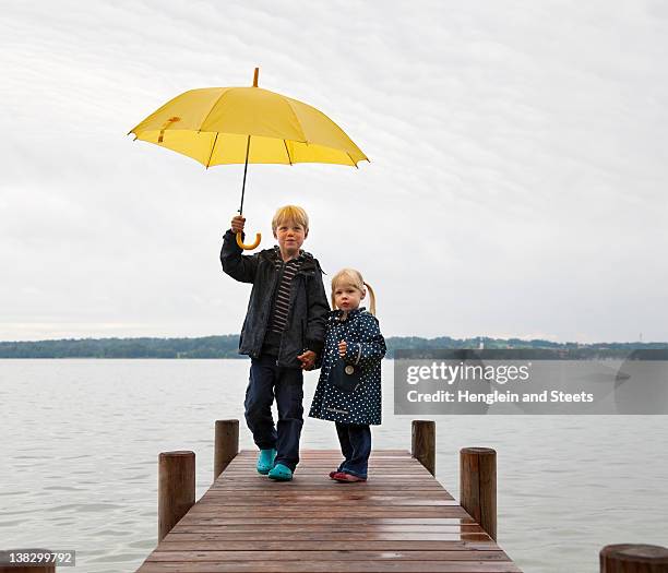 children with yellow umbrella on dock - child umbrella stockfoto's en -beelden