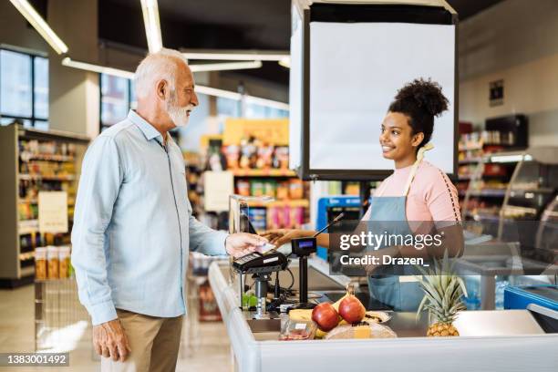 employee in supermarket serving senior customer with face mask - 收銀機 個照片及圖片檔