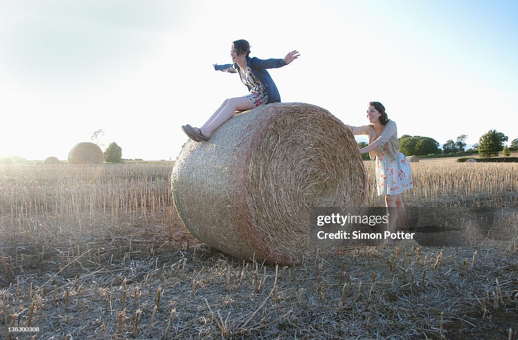 Girls playing on hay bale in field