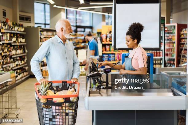 employé dans un supermarché servant un client senior avec masque facial - caisse enregistreuse photos et images de collection