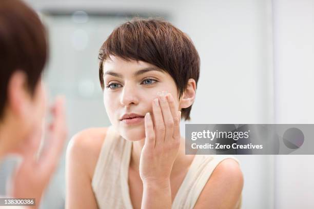 woman applying moisturizer in mirror - cream for face stock pictures, royalty-free photos & images