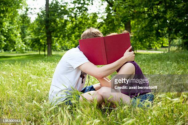 teenagers hiding behind book in park - romance book stock pictures, royalty-free photos & images