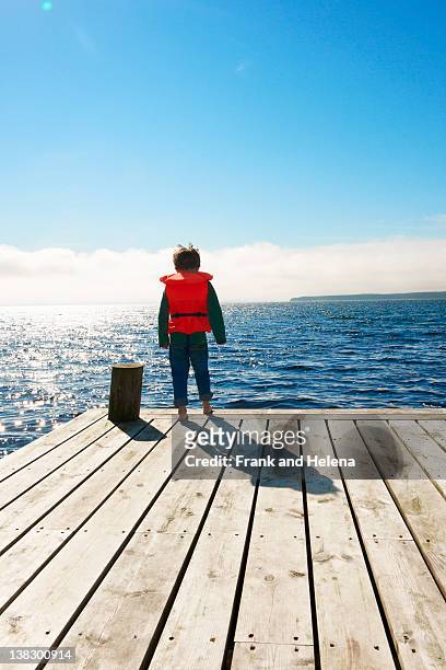 boy wearing lifejacket on wooden pier - life jacket stock pictures, royalty-free photos & images