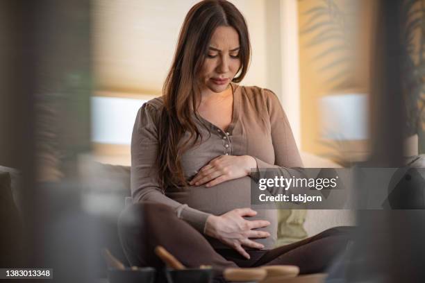 pregnant woman feeling pain while sitting in living room - giving birth stockfoto's en -beelden