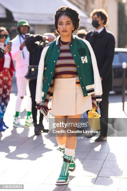 Sharon Alexie wearing a burgundy striped crop sweater, cream mini skirt, green and cream sporty jacket, yellow Louis Vuitton bag and green boots with...
