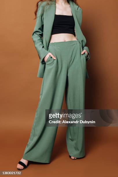 a woman poses in a new collection of clothes for sale in a green suit. women's legs and pants on a colored brown background indoors in the studio - long skinny legs foto e immagini stock