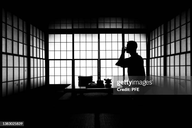 black and white indoor silhouette of japanese man taking tea. - lypsekyo16 stockfoto's en -beelden