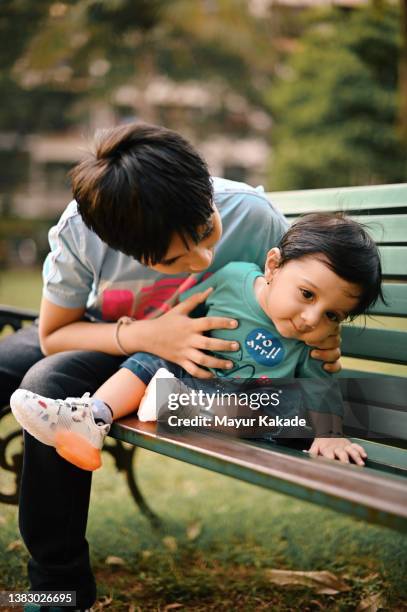 boy playing with his baby younger brother sitting on a park bench - 6 11 maanden stockfoto's en -beelden