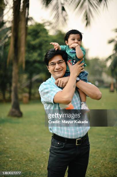 father holding his cute baby son in a park - india love stock-fotos und bilder
