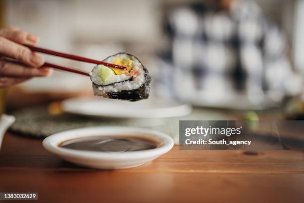 woman is dipping sushi in soy sauce - maki sushi stockfoto's en -beelden