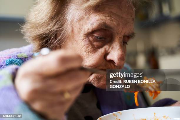 portrait of a mature woman eating spaghetti from a bowl in her kitchen. food and drink concept. - ätutrustning bildbanksfoton och bilder