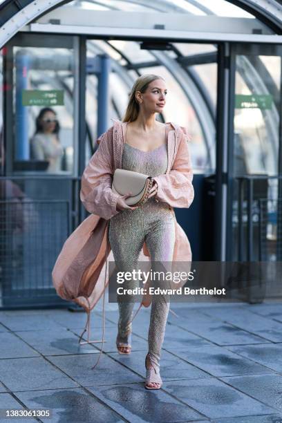 Leonie Hanne wears gold earrings, a beige tulle with embroidered rhinestones / studded V-neck / tank-top jumpsuit, a beige embossed pattern oversized...