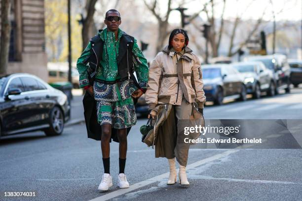 Guest wears sunglasses, a green with black and white print pattern zipper jacket, a matching green with black and white print pattern shirt, matching...