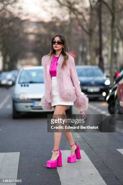 Mina Habchi wears black sunglasses from Prada, silver earrings, a neon pink with rhinestones necklace blouse, a pale pink suede with feathers borders...