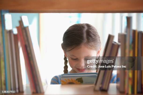 caucasian girl taking book from shelf - books on shelf stockfoto's en -beelden