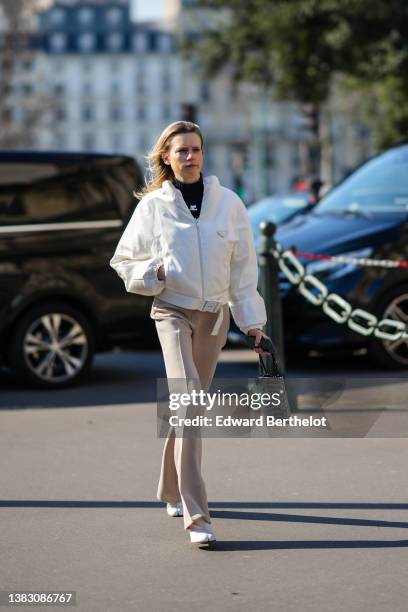 Guest wears a black turtleneck pullover from Courreges, a white jacket from Prada, beige suit pants, a black leather and silver rhinestones handbag...